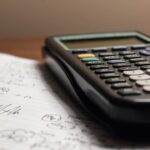 Close-up of a calculator resting on a notebook filled with mathematical calculations.