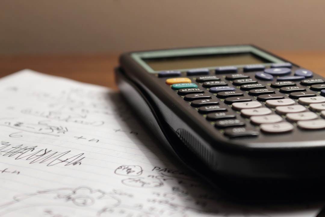 Close-up of a calculator resting on a notebook filled with mathematical calculations.