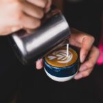 A barista pouring latte art into a cappuccino cup with a blue design