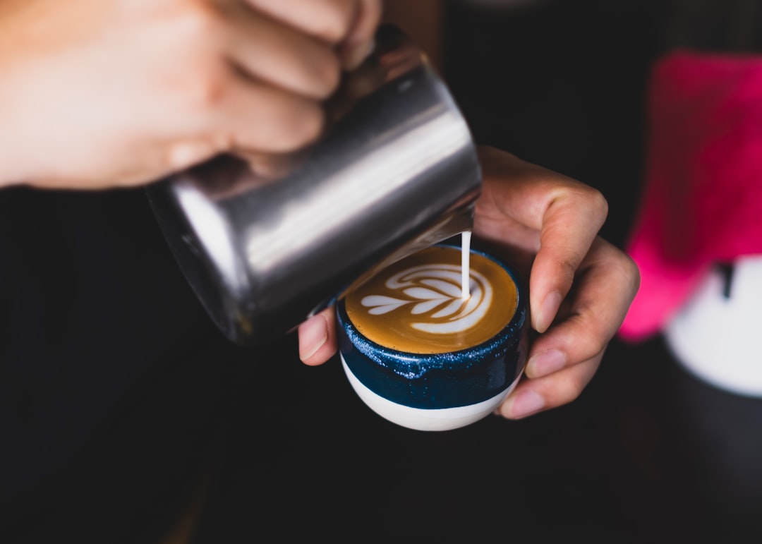 A barista pouring latte art into a cappuccino cup with a blue design